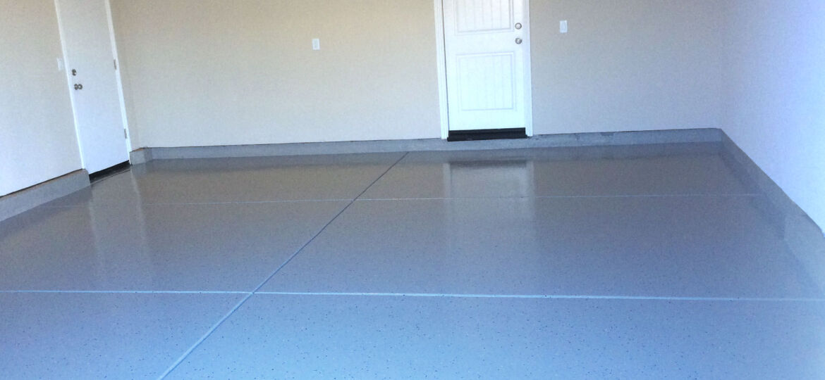 View of a clean, empty garage interior showing a freshly painted grey floor with blue speckles. The space is well-lit and features one closed white door on the left and another at the center back of the garage. A red pull-down cord for an attic staircase is visible hanging from the ceiling on the left side.