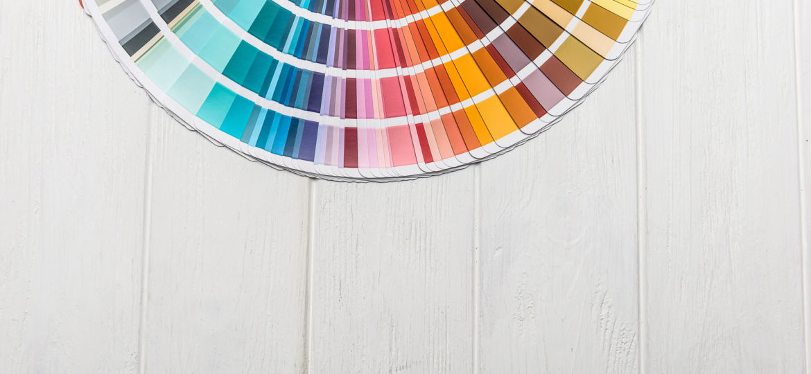 A fan deck of color swatches splayed out on a white wooden surface, showcasing an array of colors from vibrant hues to neutral tones, providing a visual selection tool for painting and design projects.
