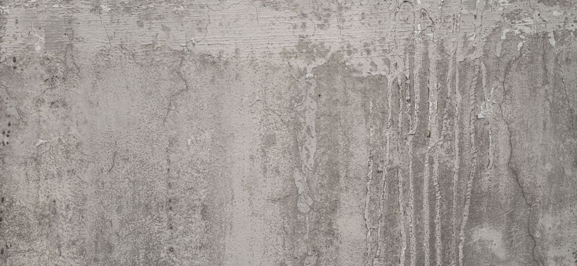 Texture of a weathered concrete wall with peeling and chipped gray paint, revealing streaks and patches of the underlying surface, indicative of decay and the passage of time.