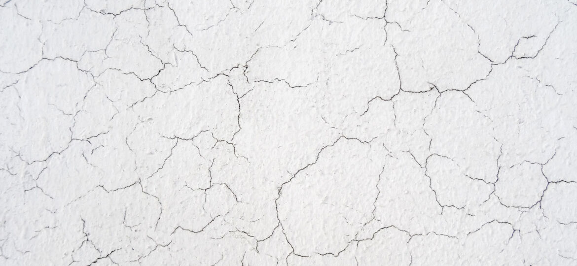 A close-up of a white, cracked paint surface creating an intricate pattern of lines and textures, indicative of aging or weathering.