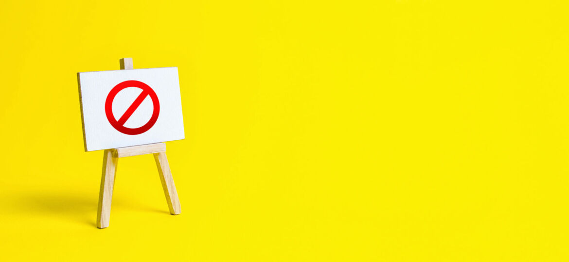 A small easel stands against a bright yellow background, holding a sign with a bold red prohibition symbol, indicating a message of restriction or a warning against certain actions.