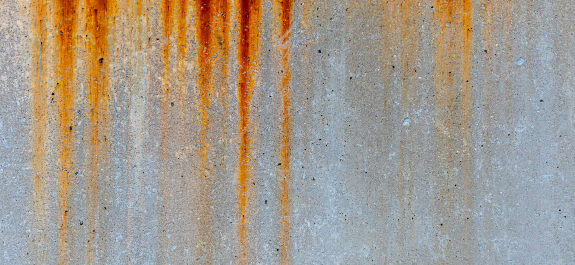 Rust streaks running down a concrete wall, showcasing the natural process of oxidation on metal elements exposed to the elements.