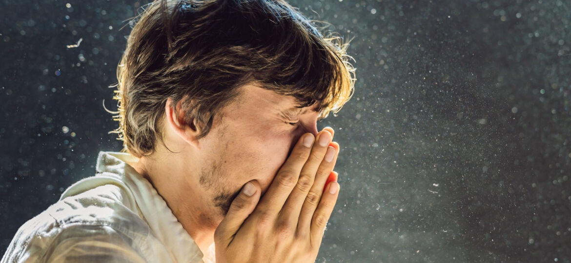 A person sneezing into their hands with visible droplets in the air, capturing a moment of common cold or allergy symptoms.