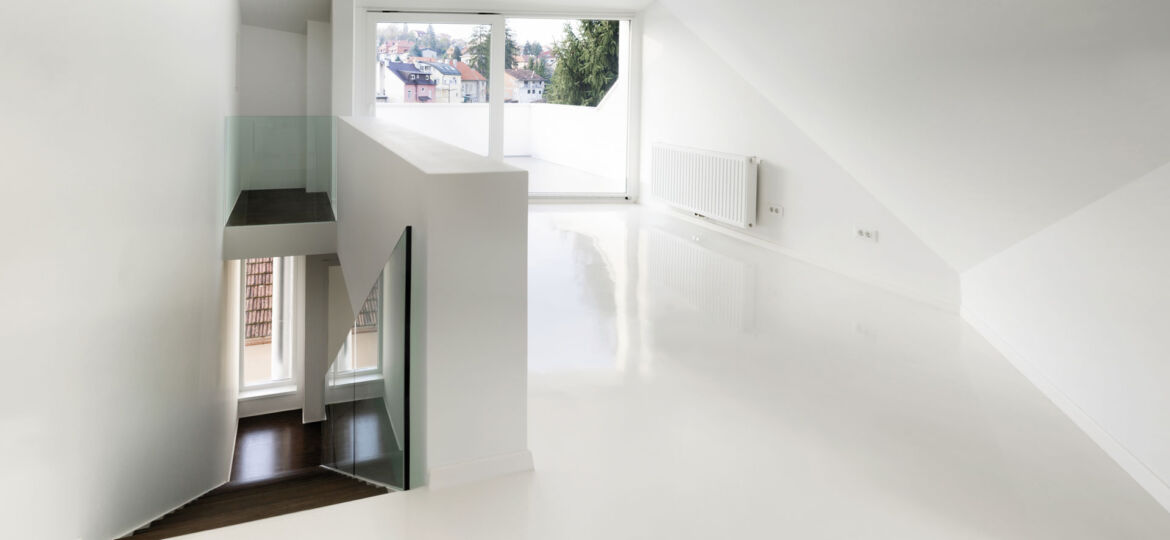 Minimalist interior of a modern home featuring white walls and a high-gloss epoxy floor, with natural light streaming through a large window offering a view of neighboring houses and trees.