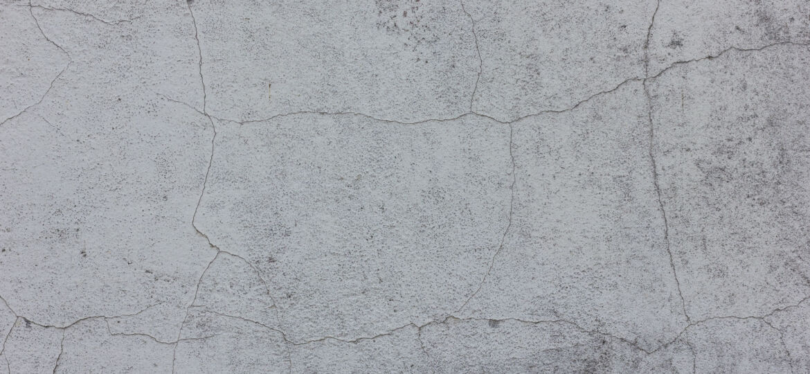 Texture of a cracked concrete wall with a detailed network of fine lines and crevices, showcasing the natural aging process and weathering effects on the surface.