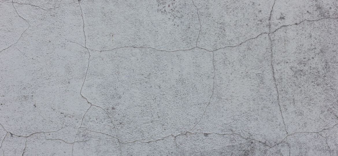 Texture of a cracked concrete wall with a detailed network of fine lines and crevices, showcasing the natural aging process and weathering or crazing effects on the surface.