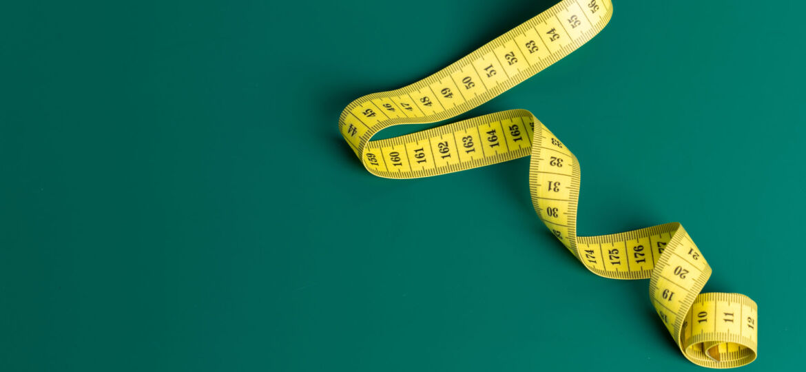 A yellow measuring tape loosely coiled against a solid teal background, creating a contrast in color as well as a sense of the tape's flexibility and utility in measuring.