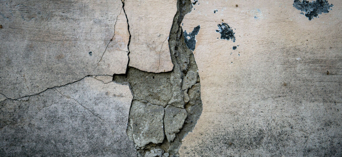 Close-up of a cracked concrete wall with peeling layers, showing signs of deterioration and the need for repair, with subtle textures and a small sprout growing from one of the cracks, symbolizing resilience.