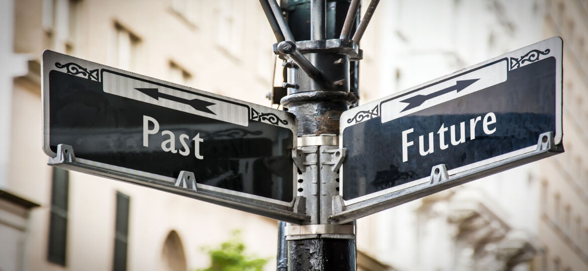 Two directional street signs mounted on a lamppost at an intersection, with one sign pointing to the left labeled 'Past' and the other pointing to the right labeled 'Future,' symbolizing a crossroads between looking back and moving forward.