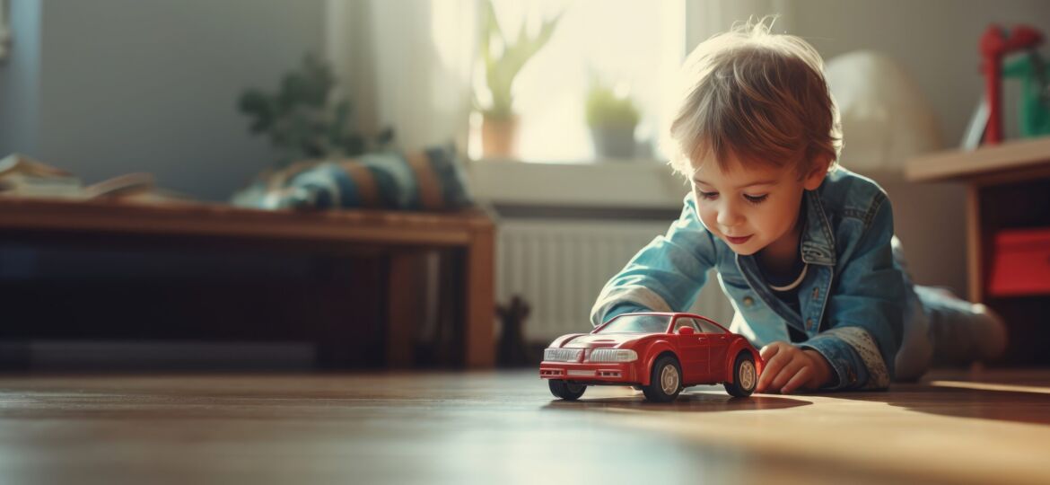 Little child laying on the floor playing with a toy car. In the background is a bench and toy box indicating it is a daycare or playroom. There are 2 green plants sitting on the window sill. Epoxy flooring is a great, safe flooring for playrooms, schools and childcare centers.