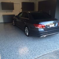 A dark gray Mercedes-Benz E-Class sedan parked on a speckled epoxy garage floor. The garage has dark cabinets with silver handles, and a closed white door is visible in the background.