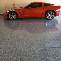 Bright red sports car parked on a glossy, polished concrete floor with a speckled finish, reflecting the vehicle's silhouette. The garage door is partially visible in the background.